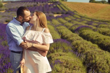 A couple in love in a field of lavender at sunset in good weather. Beautiful woman in a dress and straw panama with a man on the background of nature, love and feelings. Blue, purple lavender
