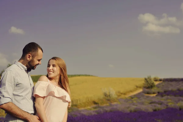 A couple in love in a field of lavender at sunset in good weather. Beautiful woman in a dress with a man on the background of nature, love and feelings. Blue, purple lavender