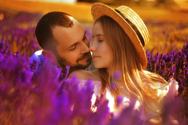 A couple in love in a field of lavender at sunset in good weather. Beautiful woman in a dress and straw panama with a man on the background of nature, love and feelings. Blue, purple lavender