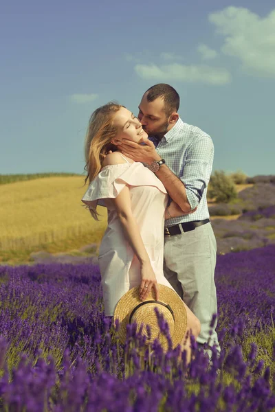 A couple in love in a field of lavender at sunset in good weather. Beautiful woman in a dress and straw panama with a man on the background of nature, love and feelings. Blue, purple lavender