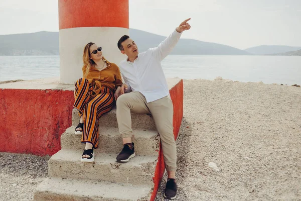 一对夫妇坐在海滩上一座灯塔旁边 面对着大海和群山 度假爱 度蜜月 时髦的夫妇 — 图库照片
