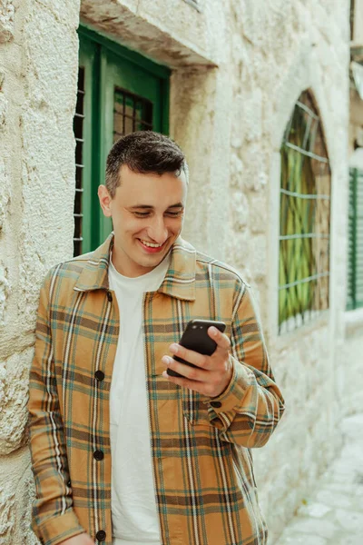 Portrait of a guy on the background of the old city with a phone. The guy writes a message and looks at the smartphone. Communication abroad, roaming, dating while traveling.