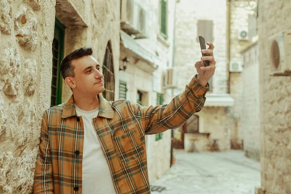 在古城背景上一个拿着电话的男人的画像 那家伙看了看智能手机 在国外交流 视频通话或自我推销 — 图库照片