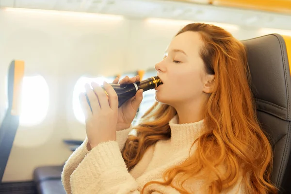 The girl drinks alcohol from duty free in the plane, fear of flying, alcohol in flight transport. Exciting trip, alcohol prices on the plane.