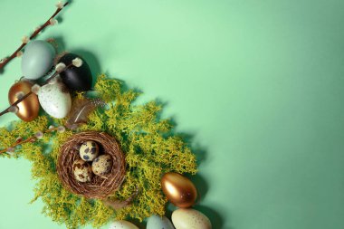 Quail eggs in a nest on natural moss, pussy willow and decorative, painted eggs. Easter celebration, stylish photo on a green background. Place for text, postcard