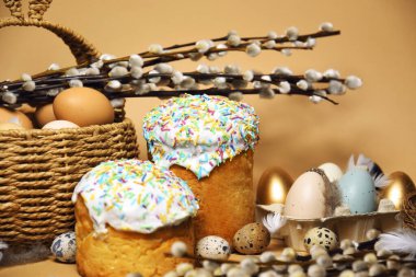 Easter holidays, pussy willow, colorful painted eggs in a tray, quail eggs in a nest, a basket with Easter cake on a nude background, warm. Religion and traditions