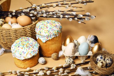 Easter holidays, pussy willow, colorful painted eggs in a tray, quail eggs in a nest, a basket with Easter cake on a nude background, warm. Religion and traditions