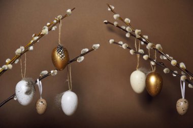 Easter decorations on a brown background. Painted eggs hang on pussy willow branches. Spring is coming, place for text