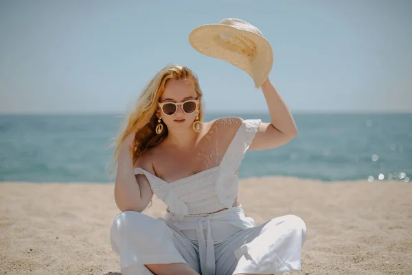 身穿白色衣服的快乐女孩坐在沙滩上 面对着大海或海滩 女人笑 时装模特 漂亮的珠宝 太阳镜 — 图库照片
