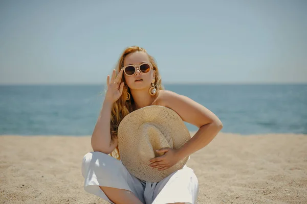 在大海的背景下 一个穿着白色衣服的时髦时髦的长腿模特坐在海滩上享受生活 夏天的心情 穿着漂亮珠宝的金发富婆 — 图库照片