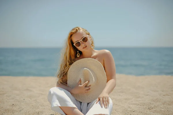 在大海的背景下 一个穿着白色衣服的时髦时髦的长腿模特坐在海滩上享受生活 夏天的心情 穿着漂亮珠宝的金发富婆 — 图库照片