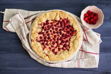 Ev yapımı ahududu pastası ya da mavi ahşap bir masa üzerinde beyaz bir bez, yanında taze böğürtlen, üst görünüm.