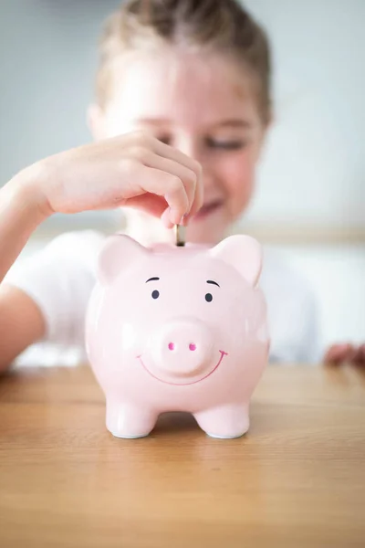 stock image Caucasian child girl putting a coin in a pink piggy bank. Saving money for kids concept. Vertical shot.