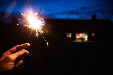 Elinizde maytap, ya da Bengal yangın çubuğu, açık havada alacakaranlıkta yanan arka planda bir ev. Tatiller veya kopyalama alanı olan sihirli duvar kağıtları.