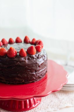 Kırmızı pasta standında çikolatalı çilekli pasta beyaz arka planda fotokopi alanı ile. Ayrıntılı, dikey çekim.