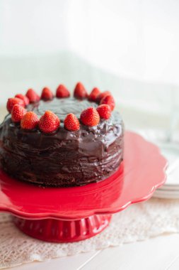 Kırmızı pasta standında çikolatalı çilekli pasta beyaz arka planda fotokopi alanı ile. Ayrıntılı, dikey çekim.