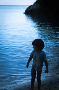 3 yaşında bir çocuk, plajda yürüyor, arka planda deniz var, kasvetli mavi filtreli bir görüntü..