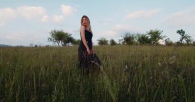Romantik kadın, siyah uzun elbiseli güzel sarışın manken elma bahçesindeki bir çayırda duruyor. Köy kavramı