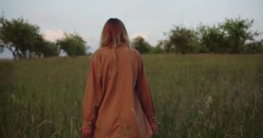 Romantik bir kadın, kahverengi gömlekli güzel bir kadın model çayırda duruyor ve yürüyor, kamera kovalıyor.