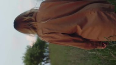 Dikey video romantik kadın, güzel sarışın model kamera önünde hareket eden uzun otların arasında yürüyor.