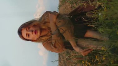 Dikey video romantik beyaz kadın çayırda oturuyor ve batan güneşin ışınlarında tarlayı sürüyor.