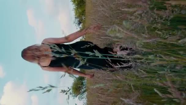 在一片草地上 身着黑色衣服的金发美女从摄像机前走出来 这段视频是垂直拍摄的 — 图库视频影像