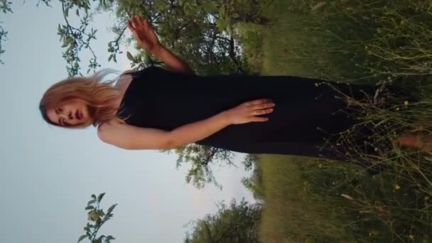 Vertikal Film Vacker Kvinna Blond Svart Klänning Stående Gräsbevuxen Trädgård — Stockvideo
