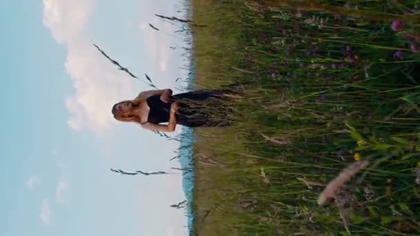 垂直的电影录影带美丽的金发女穿着黑色衣服站在草木花园里 — 图库视频影像