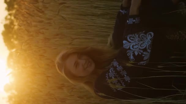 美丽的年轻女子坐在金色麦田里 闪烁着夕阳余晖的垂直画像 — 图库视频影像