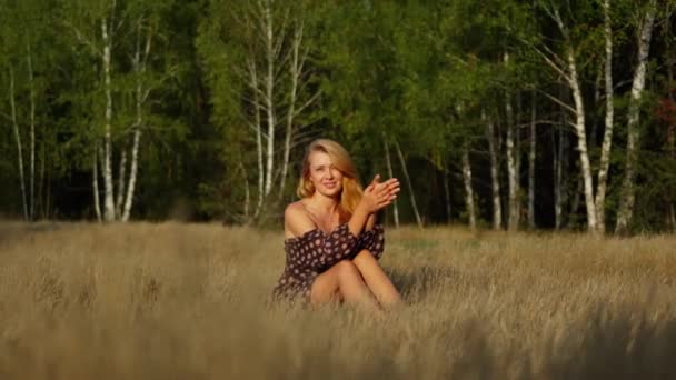 穿着点缀裙的年轻漂亮的姑娘坐在秋天的田野里 微笑着 摆着姿势 — 图库视频影像