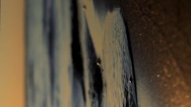 Gün batımında deniz dalgaları kumlu sahil şeridine vuruyor. Gün batımında gökyüzü dikey.