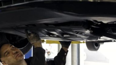 Araba tamircisi plastik araba motorunu söker ve benzin istasyonundaki aracın altında eski plastik sump koruyucuyu söker.