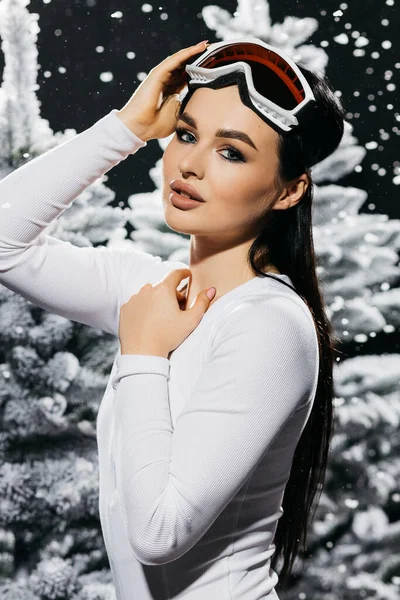 Beautiful girl in bodysuit and ski mask against a backdrop of snow-covered trees. High quality photo