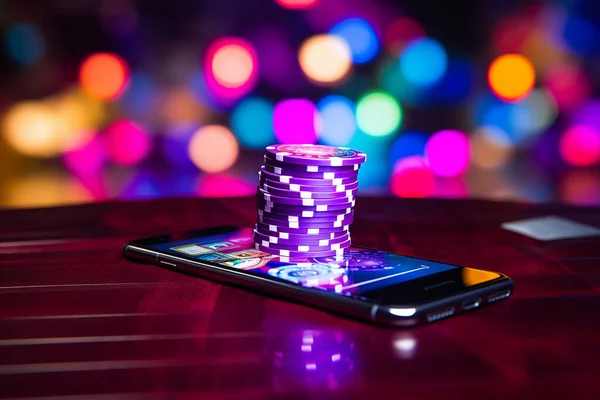 Online casino banner. Smartphone with playing chips on table on blurred neon background with bokeh effect. High quality photo
