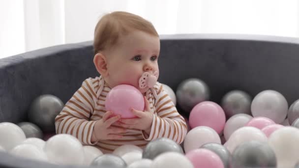 婴儿在一个满是粉色 白色和灰色球的球坑里享受着玩耍的时光 这是一个有趣而迷人的幼儿玩具 快乐的孩子玩得很开心 — 图库视频影像