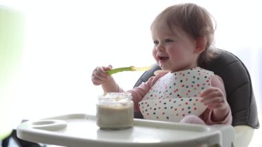 Neşeli ve mutlu bir bebek kaşıkla yemek yerken neşe içinde deneyler yapıyor.