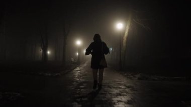 Bir kadın gecenin geç saatlerinde şehir parkında dikkatli bir şekilde yürür.