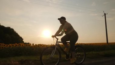 Kilolu genç bir kadın gün batımında kilo vermek için kırsalda bisiklet sürüyor..