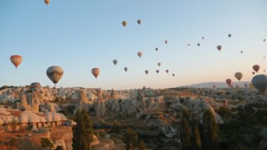 Birçok sıcak hava balonu şafak vakti Cappadocia 'nın kaya oluşumları üzerinde gökyüzüne yükselir. Gökyüzü açık ve manzara peri masalı izlenimi yaratıyor.