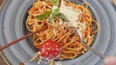 Bir tabak domates soslu spagetti, rendelenmiş parmesan ve taze otlarla süslenmiş. Tabakta bütün bir vişneli domates de var. Üst manzara bir çatal ve ahşap yemek çubuğu gösteriyor.
