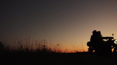 Birbirine aşık genç bir çiftin silueti gün batımıyla birlikte motosiklette oturuyor.