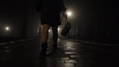 Bir bacağın alt görüntüsü, gecenin geç saatlerinde elinde çantasıyla şehir parkında yürüyen bir kadın.