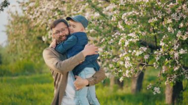 Başarılı, mutlu bir adamın portresi. Kollarında küçük oğlu çiçek açmış bir elma bahçesinde kameraya bakıp gülümsüyor.