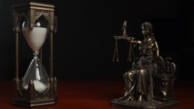 Themis 'in kılıcı ve pulu olan bir heykeli kum saatinin yanında duruyor. Karanlık arka plan, adaletin sembolizmini ve zamanın geçişini vurgulayarak dram ekler.