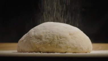 Unla kaplanmış hamurun yakın plan görüntüsü. Hamur ahşap bir yüzeyde ve arka plan karanlık.