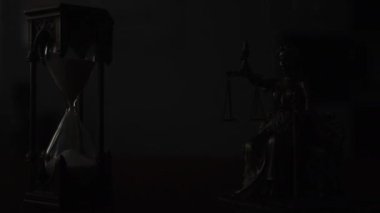 Themis 'in kılıcı ve pulu olan bir heykeli kum saatinin yanında duruyor. Karanlık arka plan, adaletin sembolizmini ve zamanın geçişini vurgulayarak dram ekler.