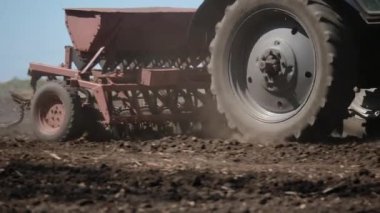 Kuru bir tarlada mısır tohumu eken traktördeki bir çiftçinin arka görüntüsü. Toz tarımsal makineyi takip ediyor. Baharda tarım işi