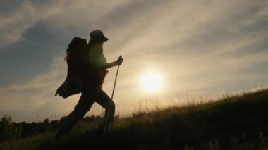 Sırt çantalı ve gün batımında sırıkla yürüyen insan silueti. Açık hava aktiviteleri doğadaki kadın konsepti