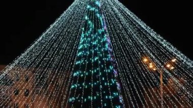 Noel Baba kırmızı takım elbiseli, beyaz sakallı, arka planda Noel ışıkları var.