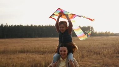 Bir anne, oğlunu tarlada omuzlarında taşır. Oğlu kafasının üstünde parlak bir uçurtma taşır. Çocuk mutlu bir şekilde gülüyor.